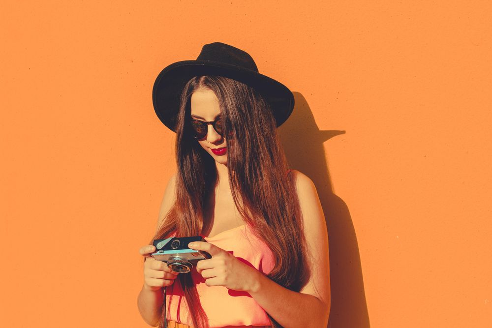 Woman wearing orange outfit and dark hat holding camera