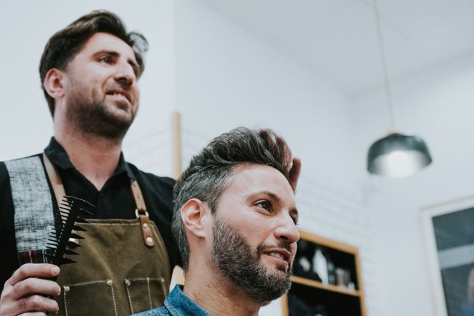 Barber combing hair to man in salon