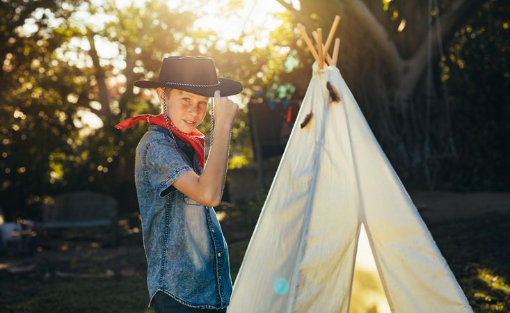 Portrait of young boy posing in cowboy hat by a backyard garden teepee