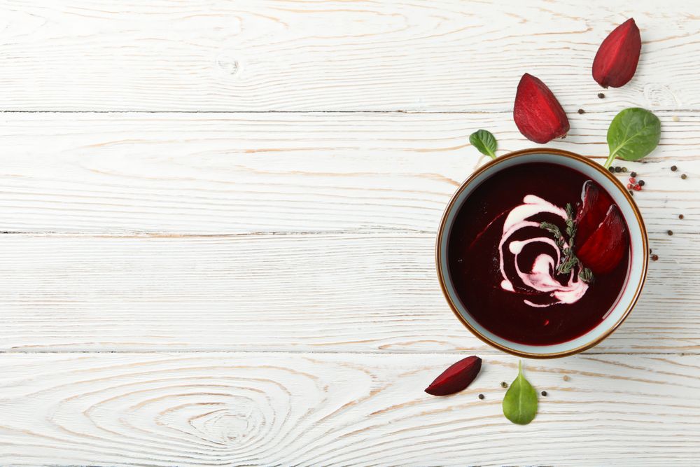 Looking down at bowl of borscht or beetroot soup on wooden table with copy space