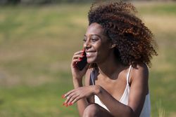 Female in light summer dress sitting in park having fun conversation on her phone