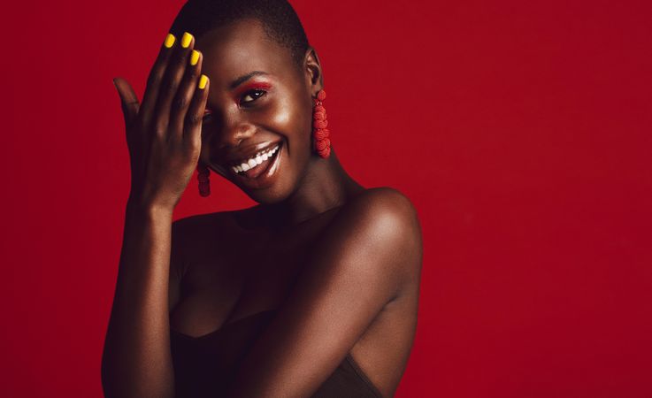 Close up of smiling African woman wearing vivid makeup against red background