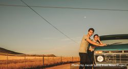 Young man and woman leaning on classic truck looking at sunset beeXpb