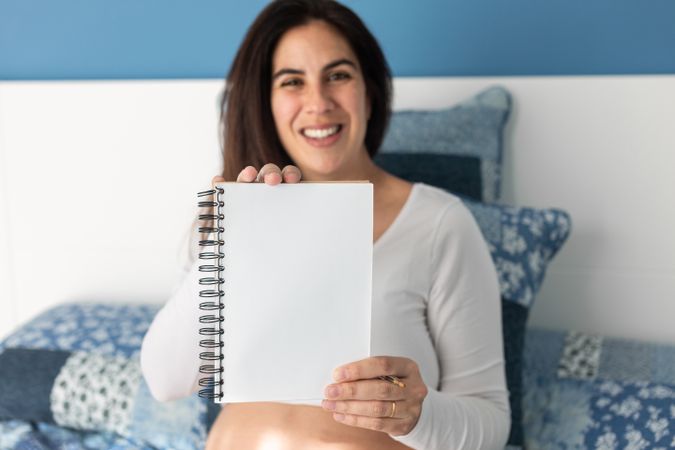 Cheerful pregnant woman showing notebook at camera