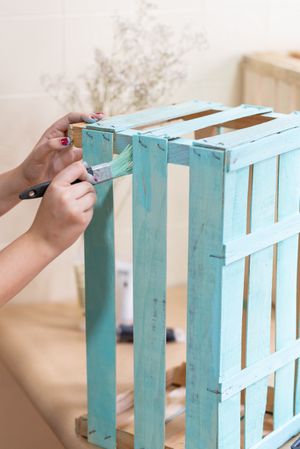 Woman paining wooden box in blue color with brush