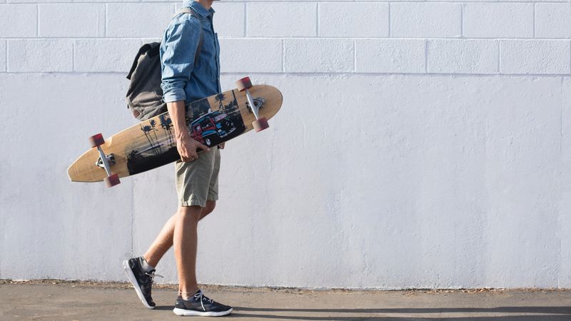 Side view of man with backpack holding a skateboard walking near wall