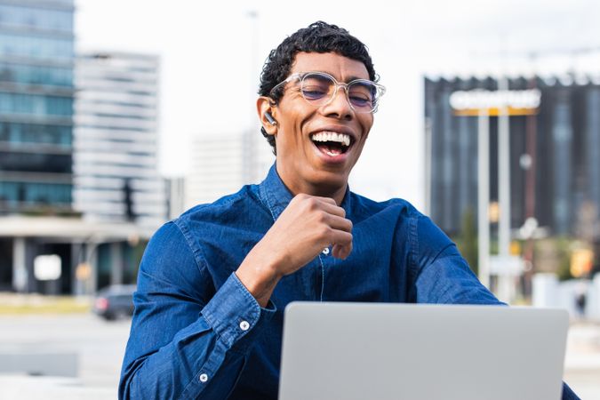 Happy hispanic male freelancer working on laptop in city