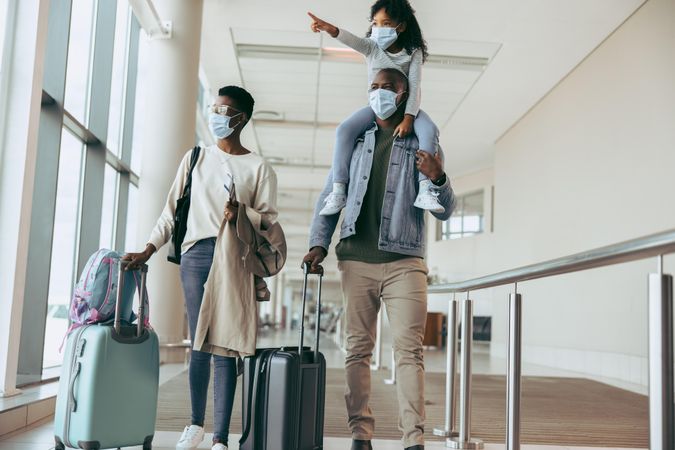 Family in pandemic with luggage at airport corridor looking away