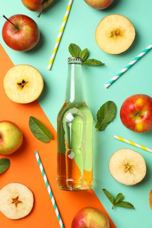 Composition with cider, apples and straws on two tone background