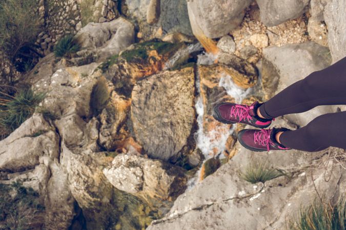 Crop female traveler legs on stone over rocky mountain