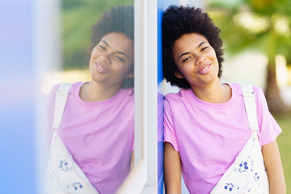 Happy woman looking at camera and leaning her side on blue building
