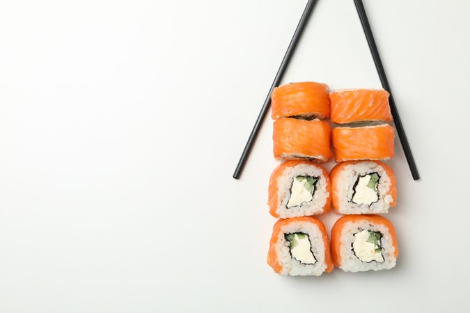 Chopsticks and sushi rolls on plain background, space for text