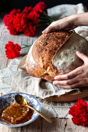 Crop person putting sourdough bread near flowers and honey