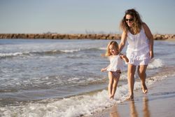 Mother and daughter playing on the seashore, running along the beach
