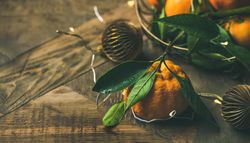 Freshly picked tangerines with leaves on wooden table, with gold Christmas decorations, copy space