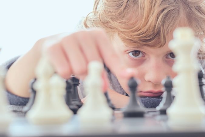 Calm preteen boy touching pawn on chess board