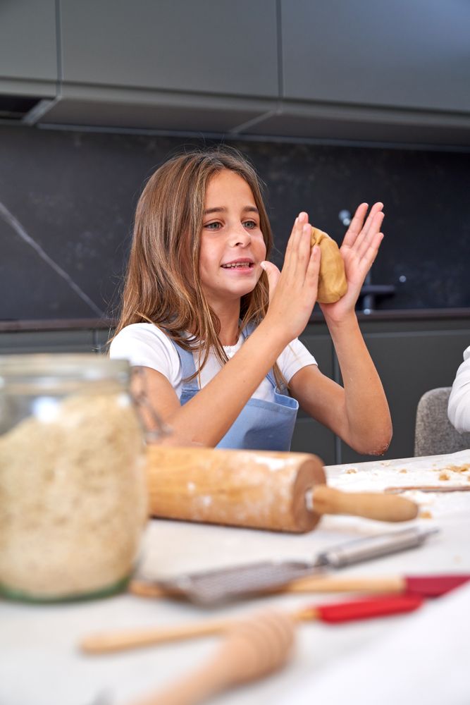 Smiling little girl kneading dough with hands in kitchen