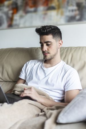 Man relaxing on sofa using laptop at home