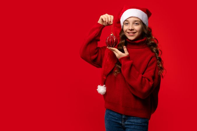 Smiling teen girl in Santa hat holding red Christmas ornament.