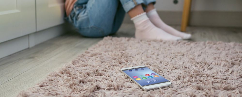 Mobile phone lying on the floor with unrecognizable sad little girl sitting behind