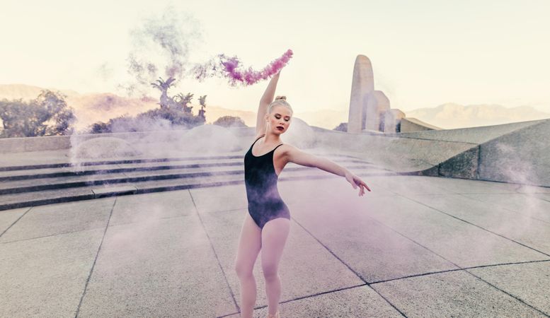 Ballet artist practicing dance moves outdoors using a pink smoke bomb