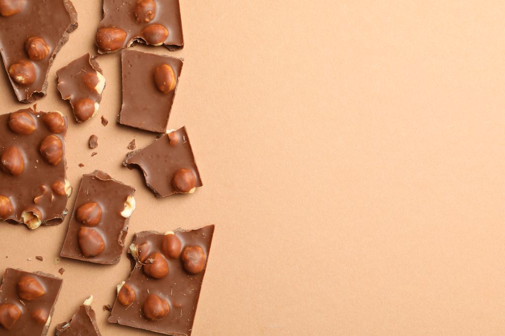 Chocolate pieces on beige background, top view. Sweet food