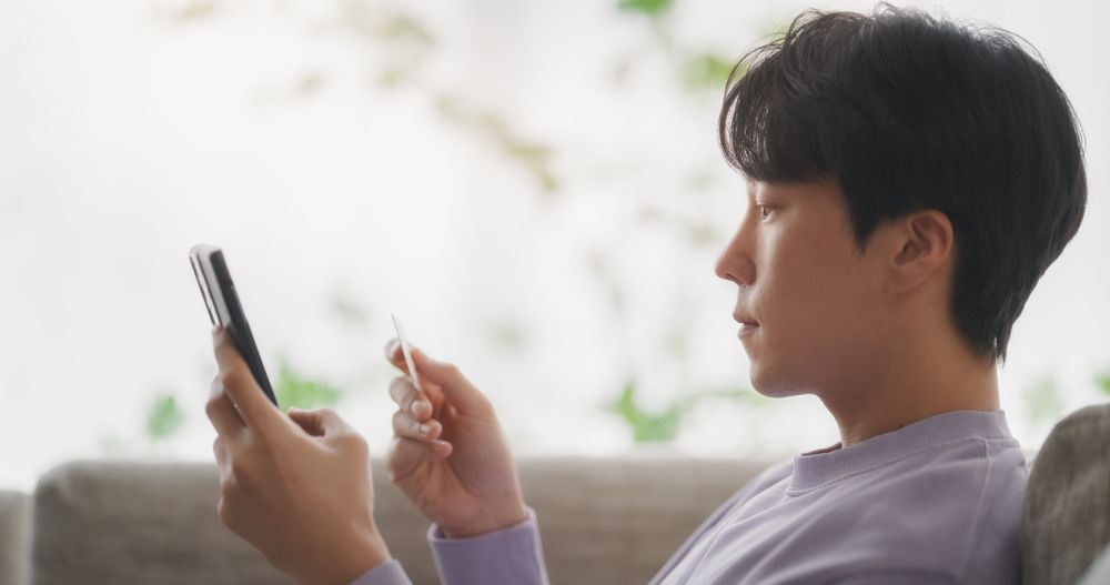 Young South Korean Man Navigating Online Shopping App in a Cozy Apartment