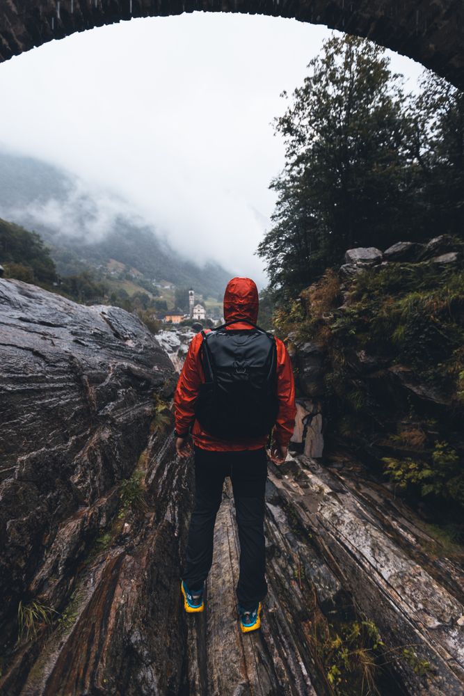 Back view of a man in red jacket with backpack walking under bridge