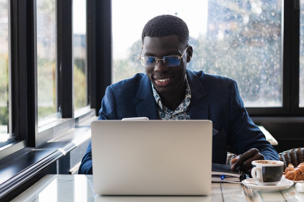 Stylish Black executive with smartphone and laptop in cafe