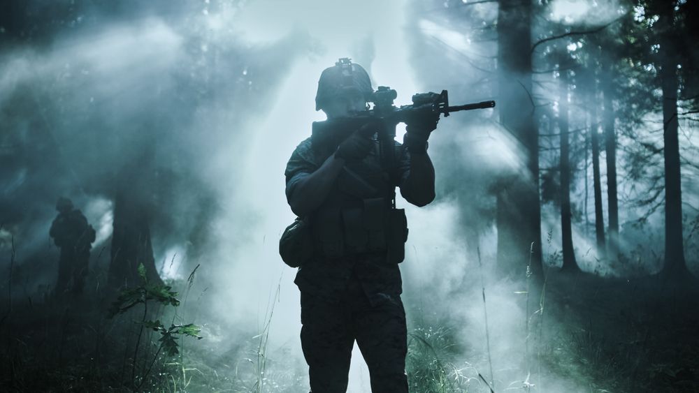 Silhouette of the Fully Equipped Soldier Moving Through Smokey Forest with Rifle Ready To Shoot.