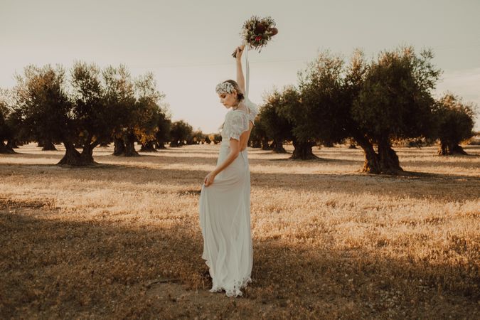 Content woman in dress with open back raising hands with flower bouquet