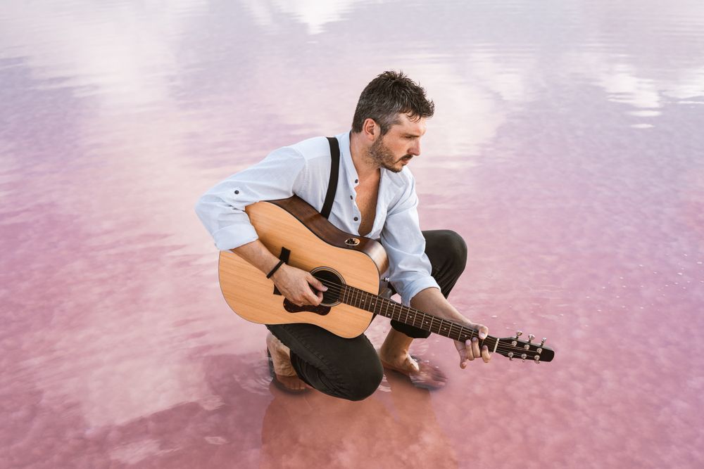 Musician with guitar on pink sandy water