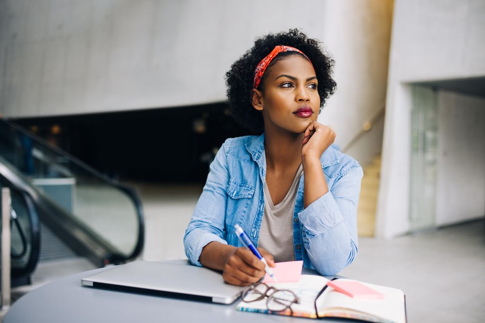 Woman thinking between writing notes in an open workspace