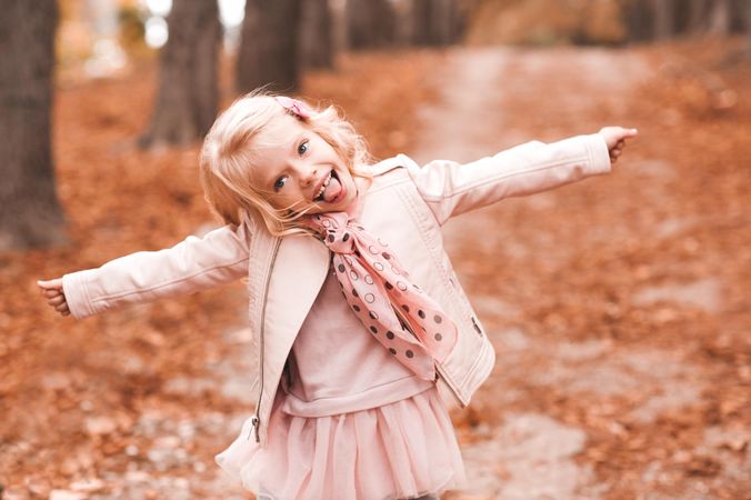 Girl in pink outfit standing on autumn tree leaves