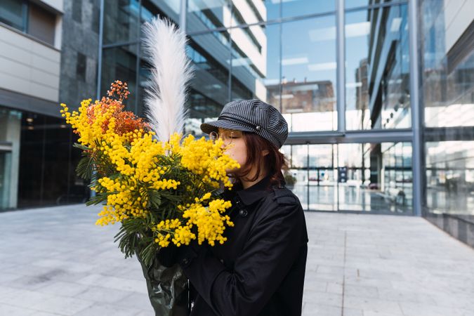 Stylish female smelling flowers on street