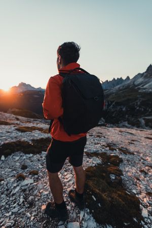 Back view of man in red jacket with backpack walking in the mountains at sunset
