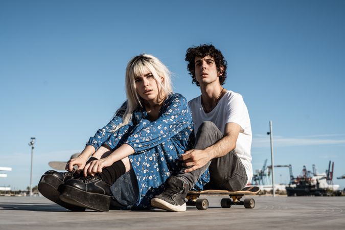 Trendy couple sitting together on skateboard on street