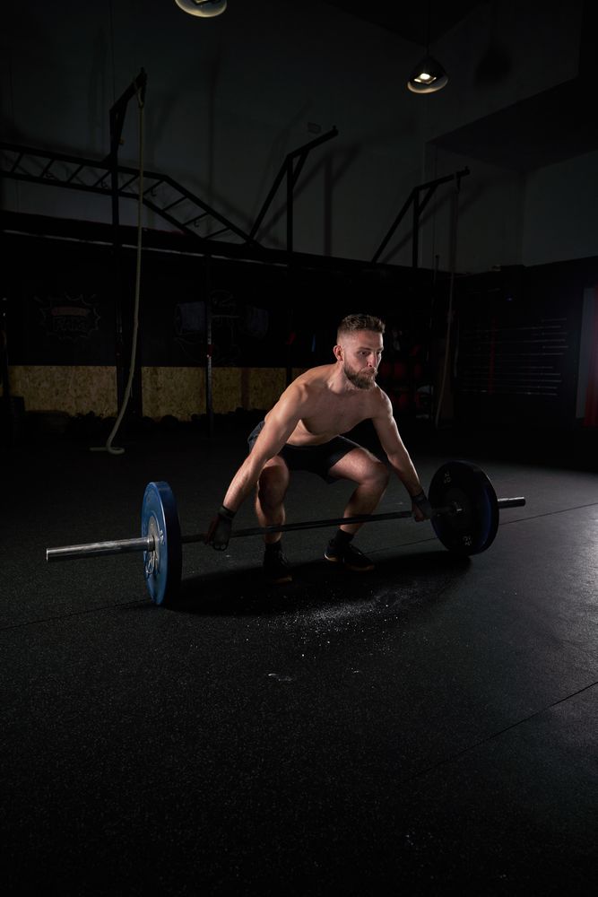 Young strong sportsman doing exercises with barbell with weights