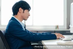 Side view of Asian male in suit at work computer bG73ab