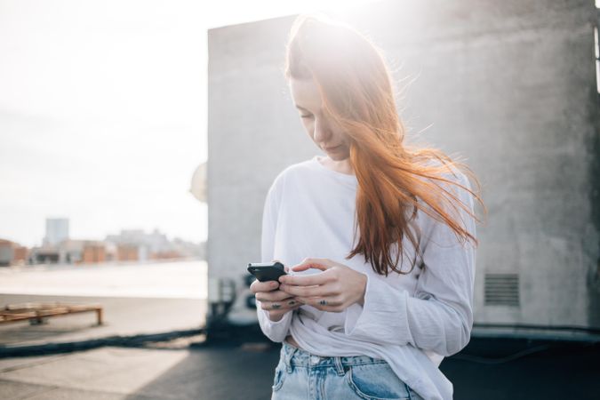 Red haired woman with her smart phone on roof