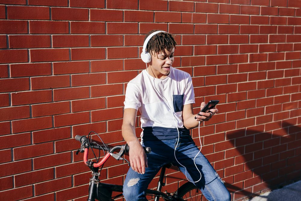 Young happy Black male listening music with smartphone on bike