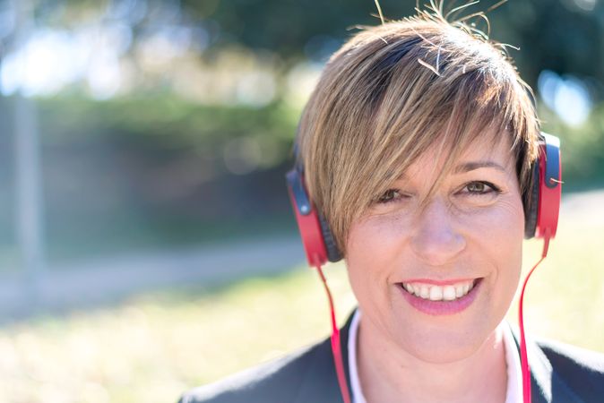 Smiling woman sitting outside listening to something on red headphones