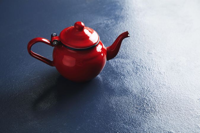 Shiny red tea pot on blue table