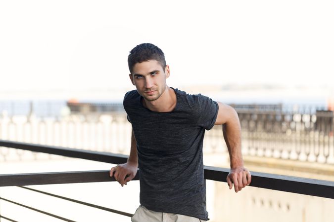 Male leaning on handrails on top of building looking at camera