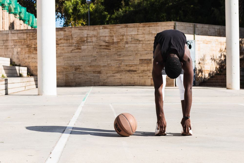 Black sportsman stretching on basketball court