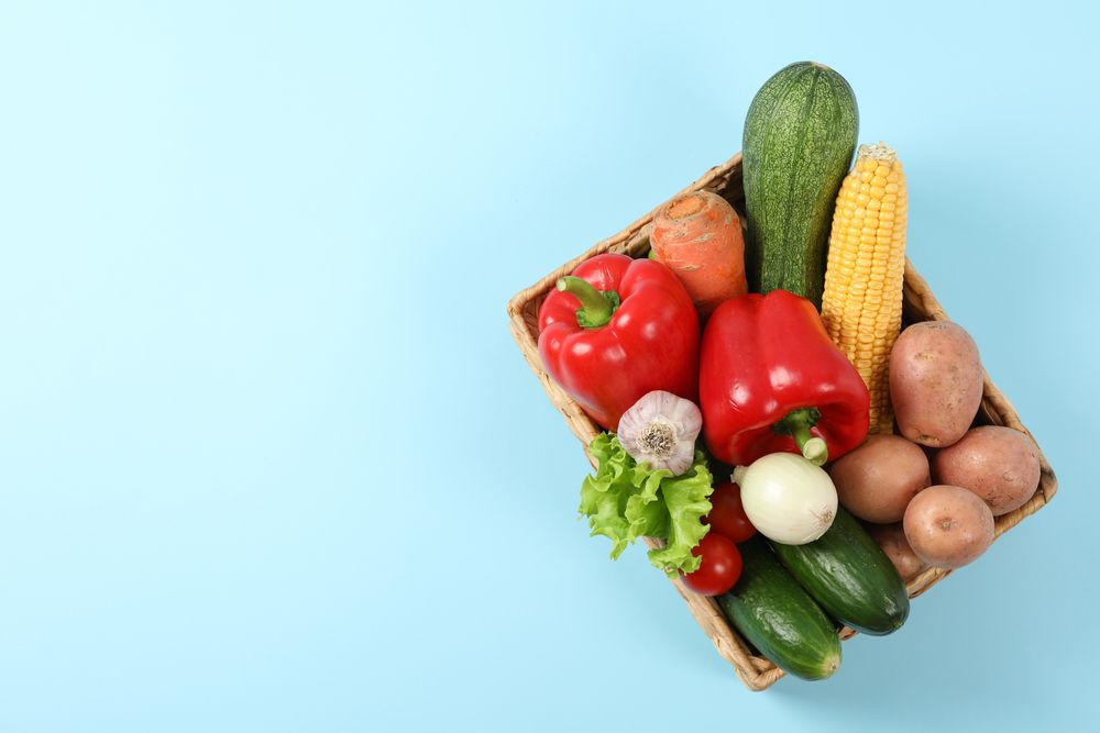 Wicker basket with vegetables on blue background, copy space