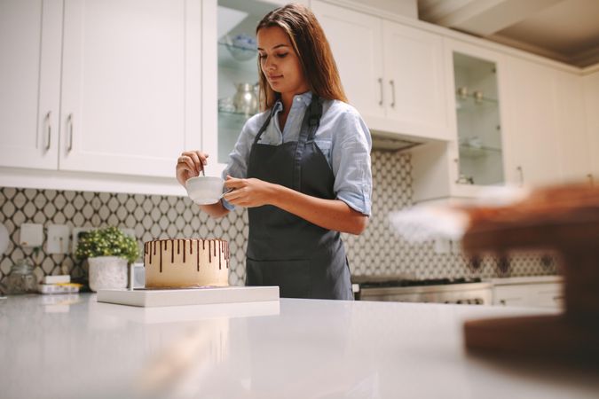 Female in apron stirring sauce in mug for cake