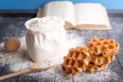Fresh waffles and ingredients with cookbook on rustic table