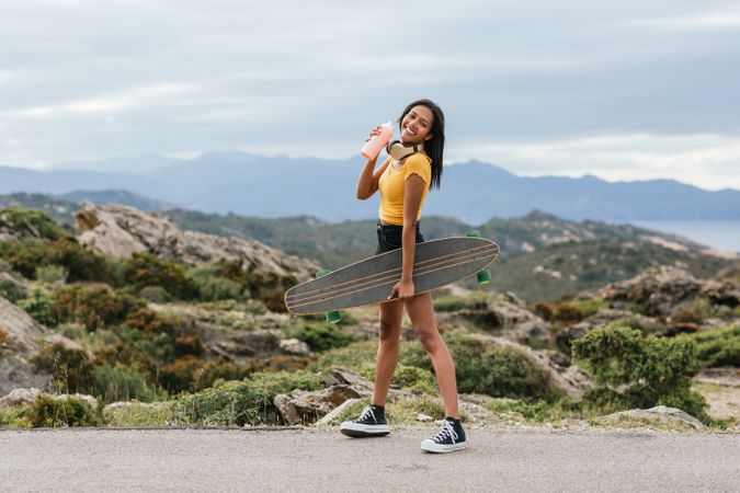 Smiling skater with longboard walking on pavement against mount
