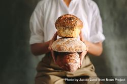 Cropped shot of chef holding various types of loaf bread against gray background 5zEjN0